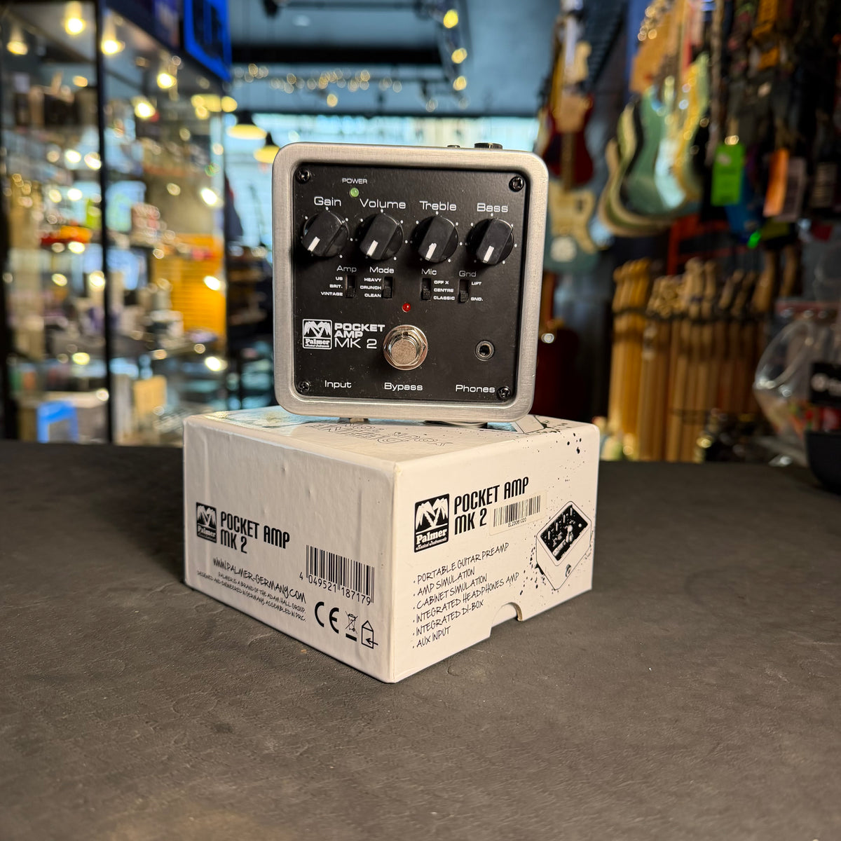 Pocket AMP MK2 guitar effects pedal on a box with a music store background